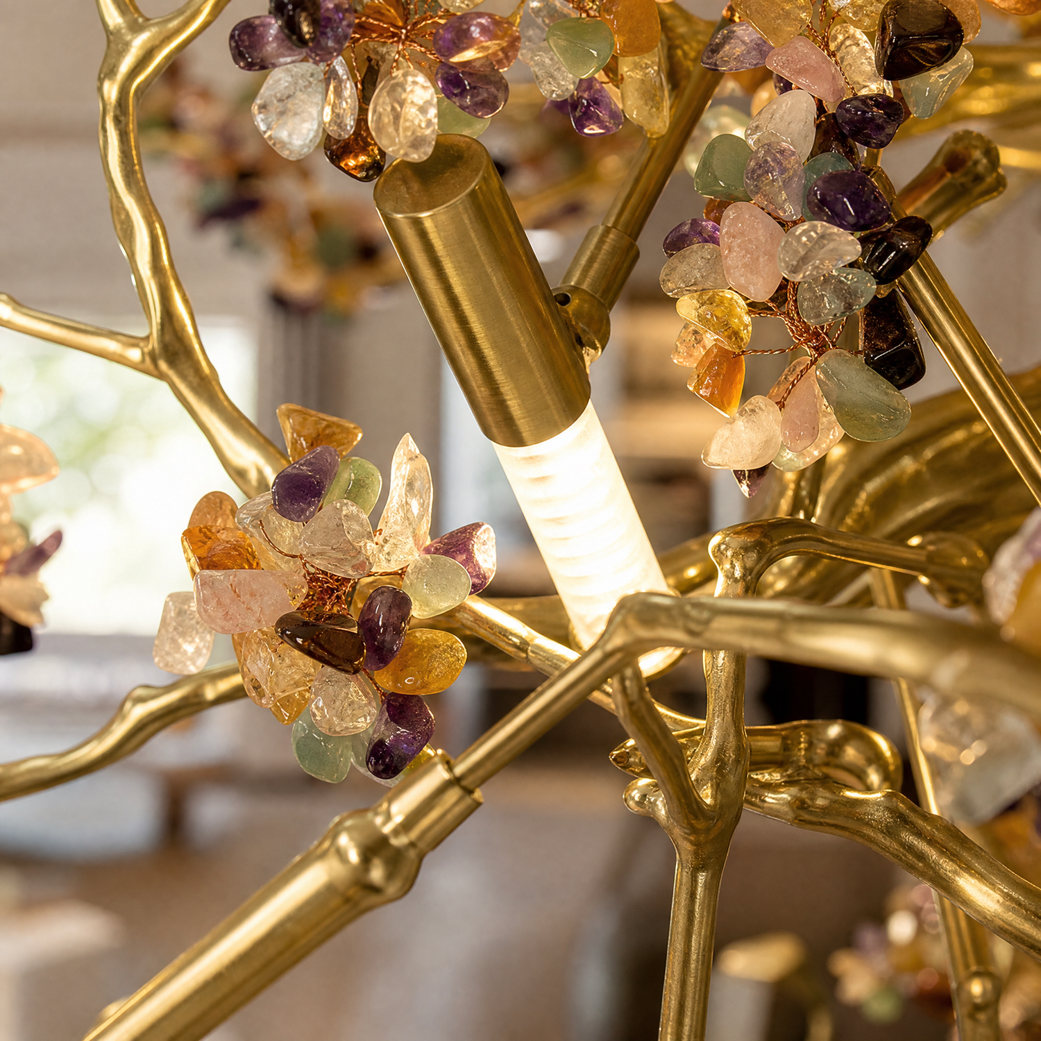 A Yiosi gold branch chandelier features a brushed brass frame with multicolored gemstone clusters and integrated downlights.
