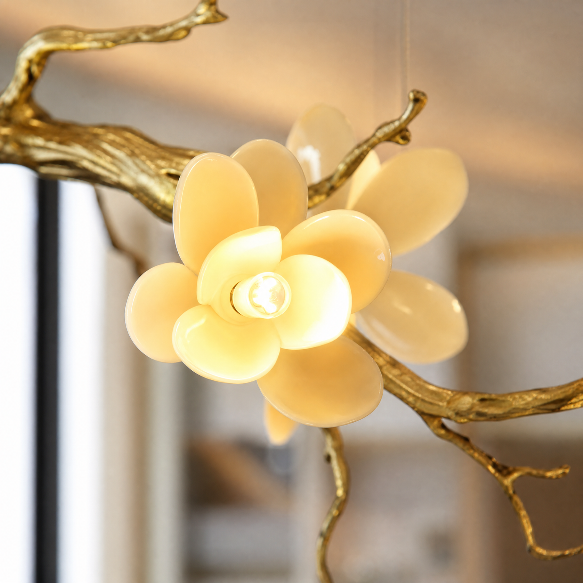 A gold metal tree branch chandelier with frosted glass floral shades hanging against a neutral background.