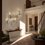 A golden branch wall sconce with cascading crystal icicles and blue and amber glass accents mounted on a neutral wall.