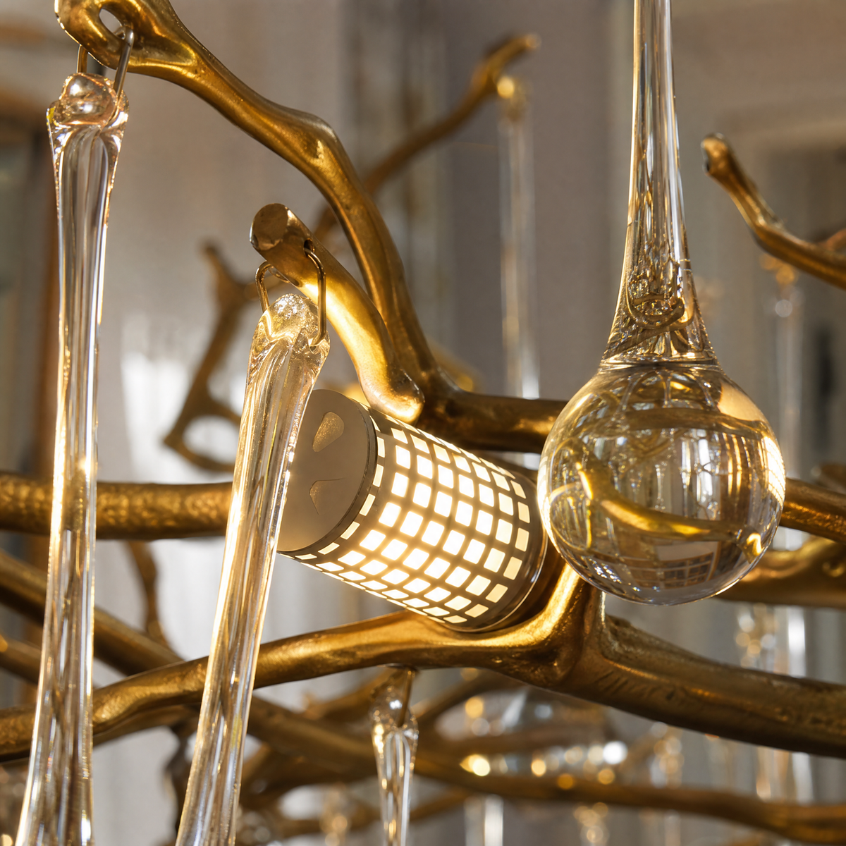 A gold metal branch chandelier with hanging clear crystal raindrops suspended by cables in a room.