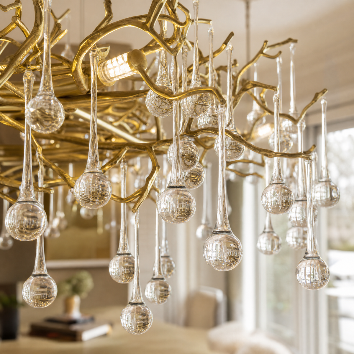 A gold metal branch chandelier with hanging clear crystal raindrops suspended by cables in a room.
