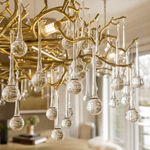 A gold metal branch chandelier with hanging clear crystal raindrops suspended by cables in a room.