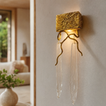 A textured gold metal wall sconce with organic branch accents and elongated fluted clear crystal pendants.