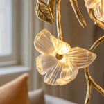 A gold metal wall sconce with a sculptural orchid floral motif and clear frosted glass accents in a triangular silhouette.