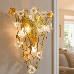 A gold metal wall sconce with a sculptural orchid floral motif and clear frosted glass accents in a triangular silhouette.