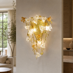 A gold metal wall sconce with a sculptural orchid floral motif and clear frosted glass accents in a triangular silhouette.