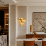 A gold metal wall sconce with a sculptural orchid floral motif and clear frosted glass accents in a triangular silhouette.