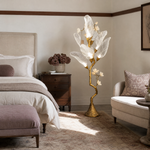 A sculptural floor lamp with a textured antique gold tree branch base and frosted glass leaf-shaped shades.