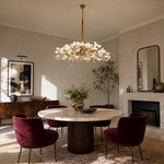 A large circular chandelier featuring numerous white ceramic ginkgo leaves and a gold metal frame hanging from a ceiling.