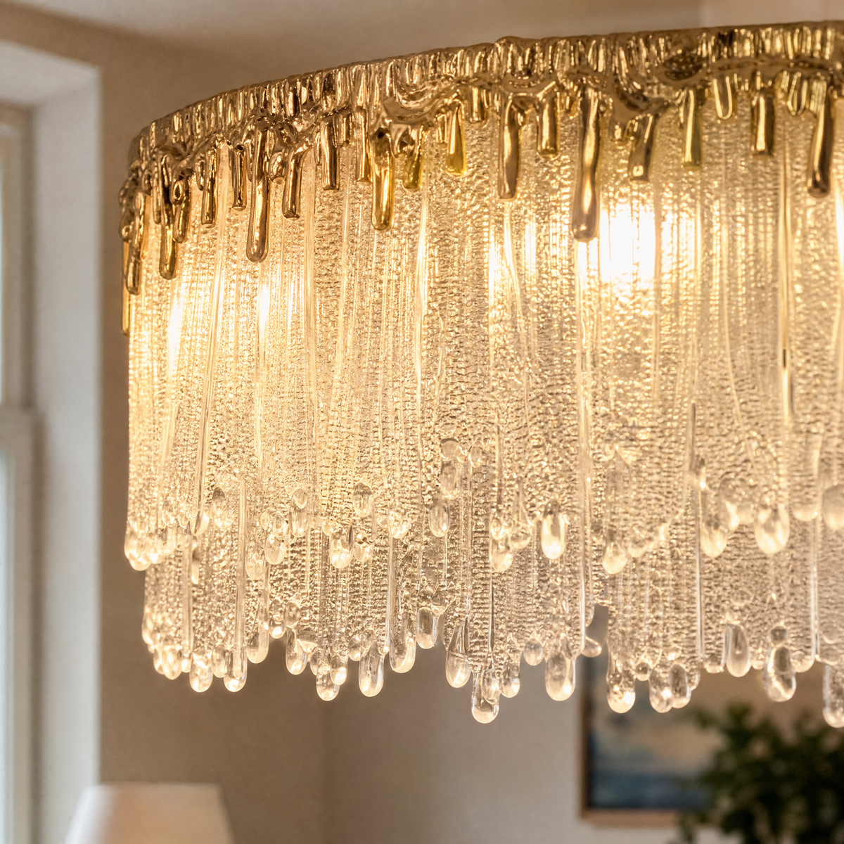 An oval crystal fringe chandelier with a warm gold textured metal band and multiple tiers of frosted icicle glass rods.