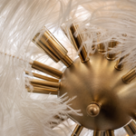 A round pendant chandelier featuring layers of white ostrich feathers and brushed brass hardware hanging in a modern space.