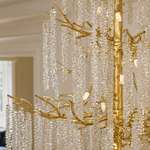 A large gold branch chandelier with tiered cascading crystal raindrop strands hangs against a neutral background.