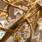 A tall gold cascading chandelier featuring metallic branches and crystal glass blossoms hanging in a high-ceiling space.