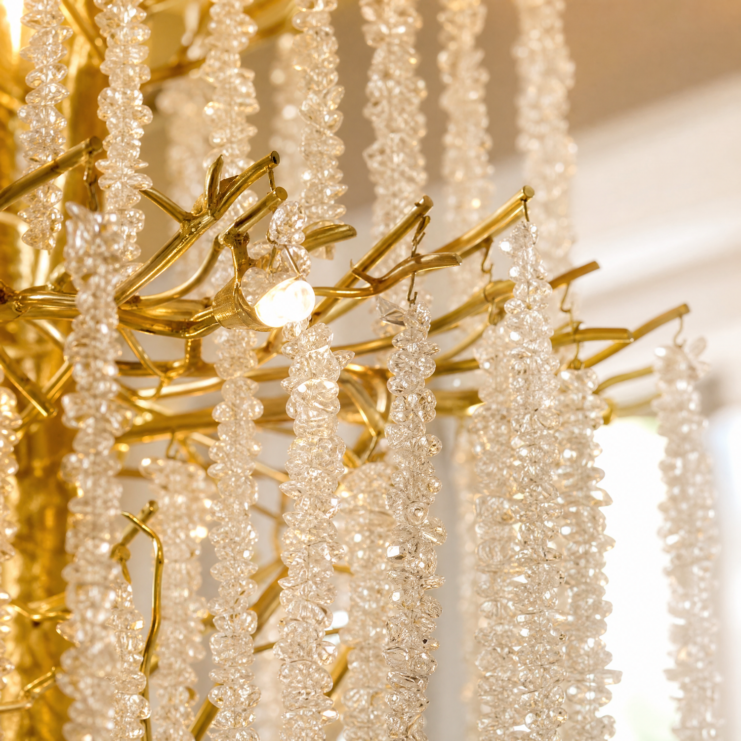 A large, multi-tiered chandelier with a gold branch-like frame and long strands of cascading crystal droplets.
