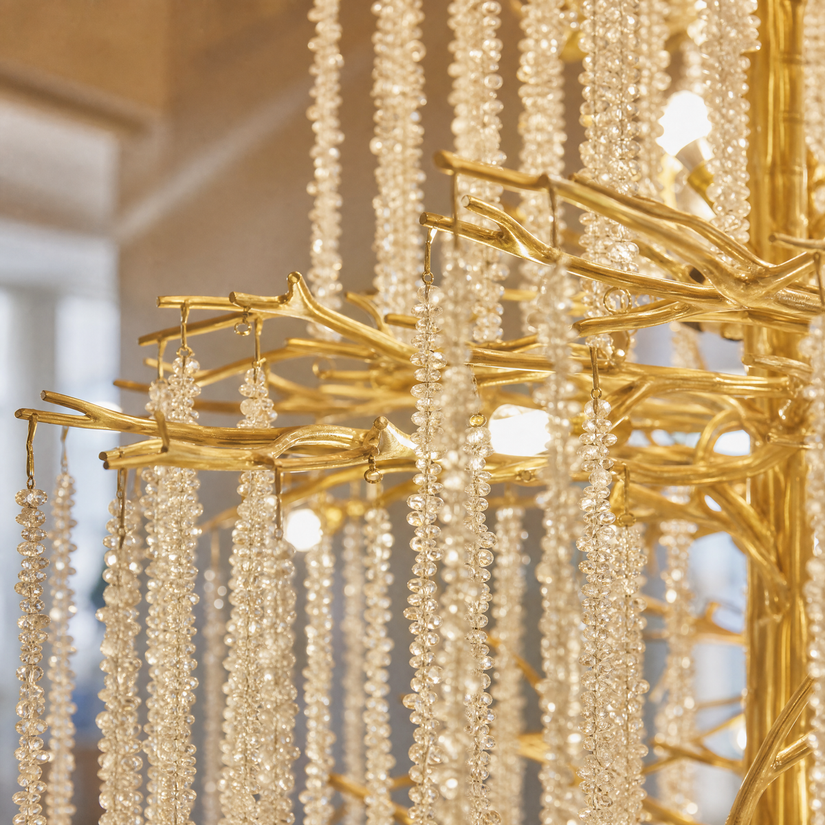 A large, multi-tiered chandelier with a gold branch-like frame and long strands of cascading crystal droplets.
