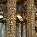 A circular antique gold branch chandelier with cascading crystal bead strands hangs from the ceiling in a lit room.