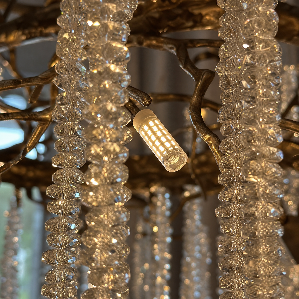 A circular antique gold branch chandelier with cascading crystal bead strands hangs from the ceiling in a lit room.