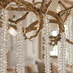 A circular antique gold branch chandelier with cascading crystal bead strands hangs from the ceiling in a lit room.
