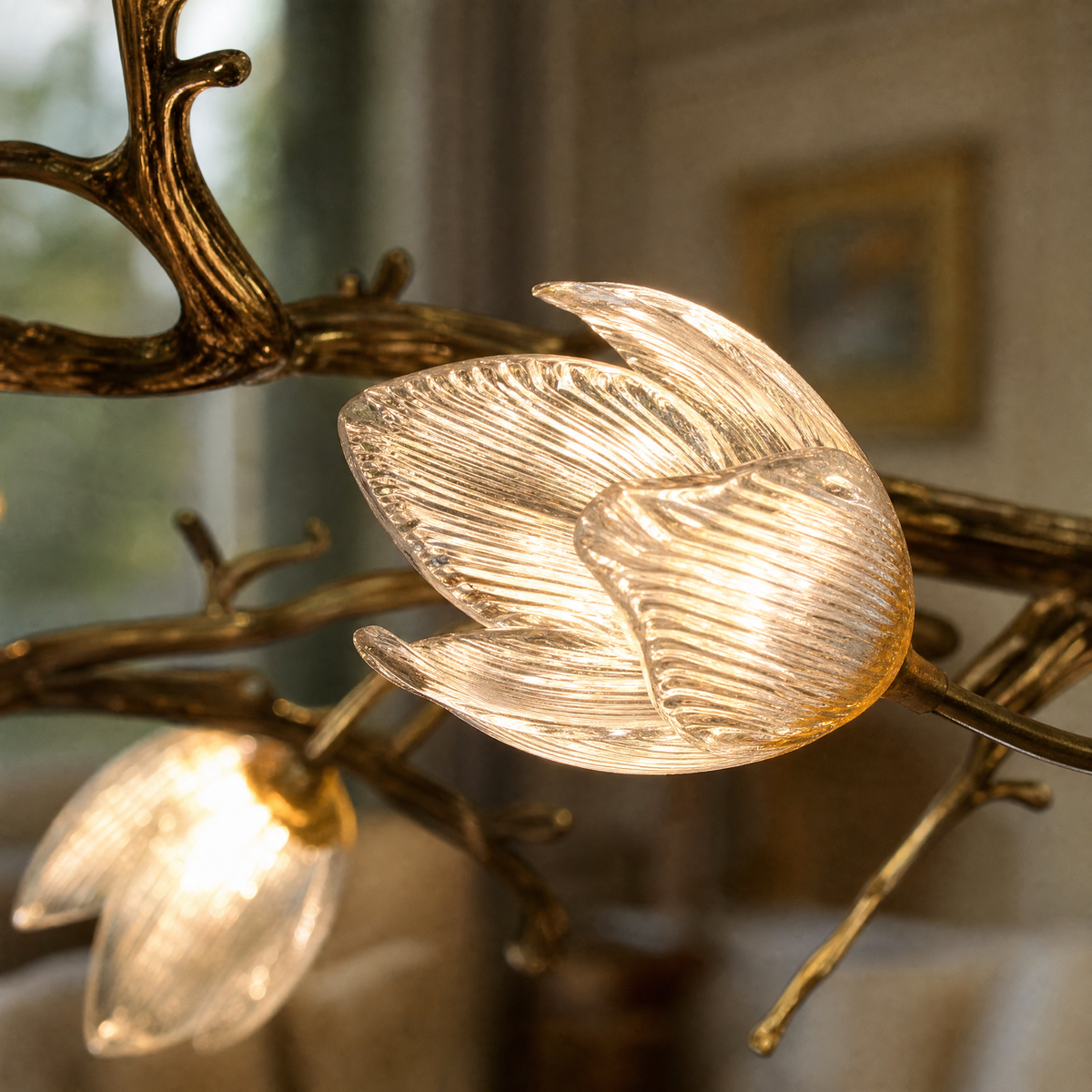 An antique brass chandelier with metal tree branches and frosted glass magnolia blossom shades suspended by multiple cables.