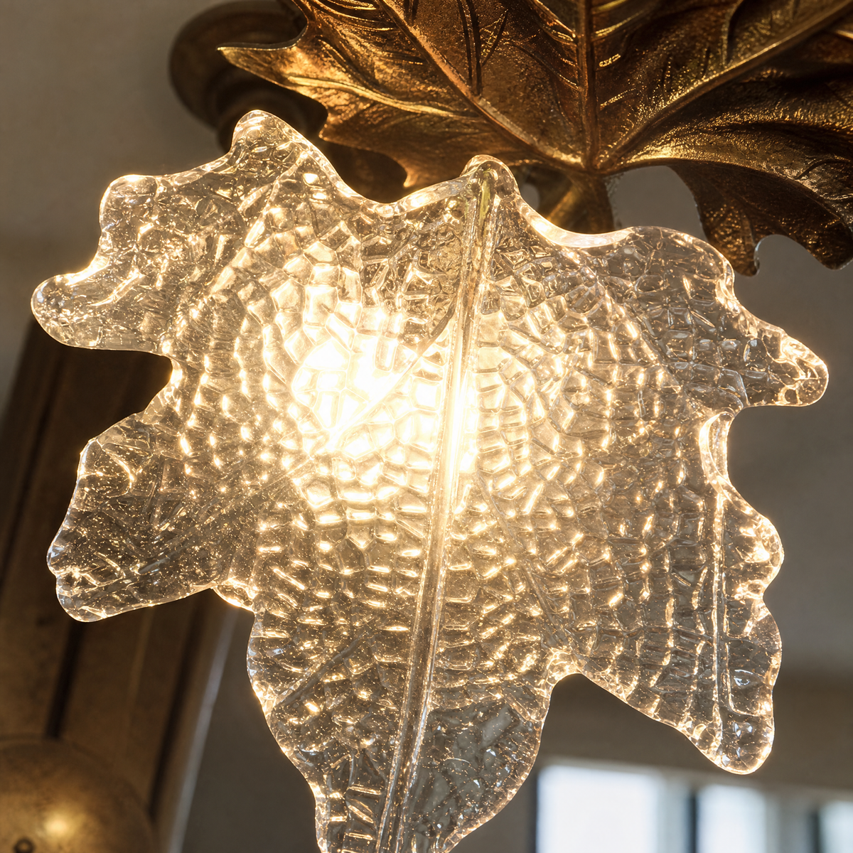 A contemporary wall sconce with a gold metal maple leaf backplate and a textured clear ice-crystal glass shade.
