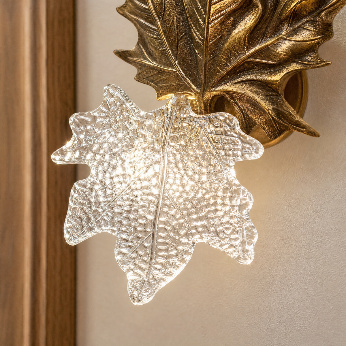 A contemporary wall sconce with a gold metal maple leaf backplate and a textured clear ice-crystal glass shade.