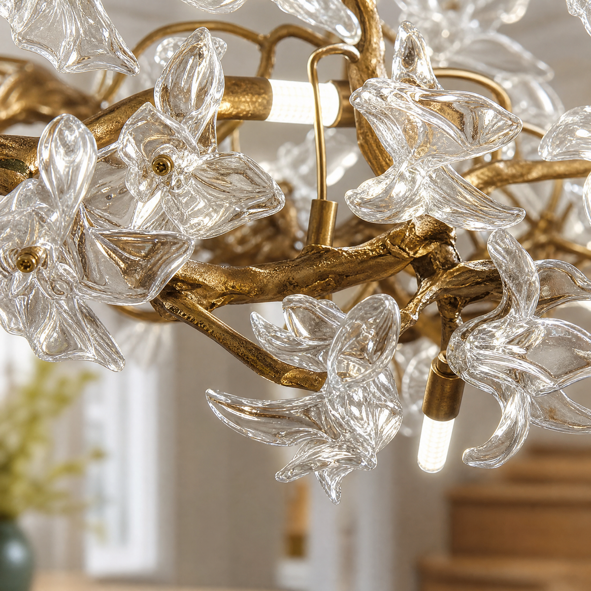 A modern organic chandelier features a warm antique brass branch frame decorated with twelve clear sculpted glass blossoms.
