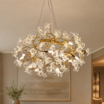 A modern organic chandelier features a warm antique brass branch frame decorated with twelve clear sculpted glass blossoms.