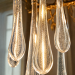 An elongated gold metal branch chandelier with hanging clear seeded glass raindrop accents in a modern dining room.