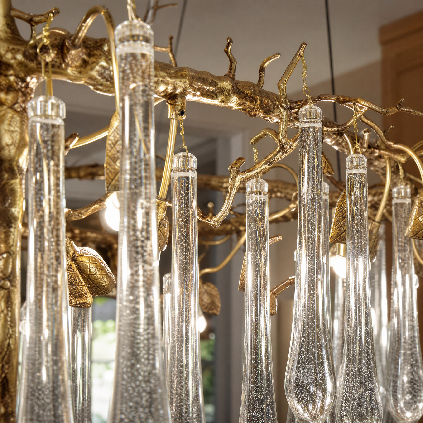An elongated gold metal branch chandelier with hanging clear seeded glass raindrop accents in a modern dining room.