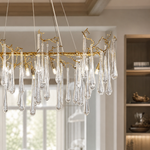 An elongated gold metal branch chandelier with hanging clear seeded glass raindrop accents in a modern dining room.