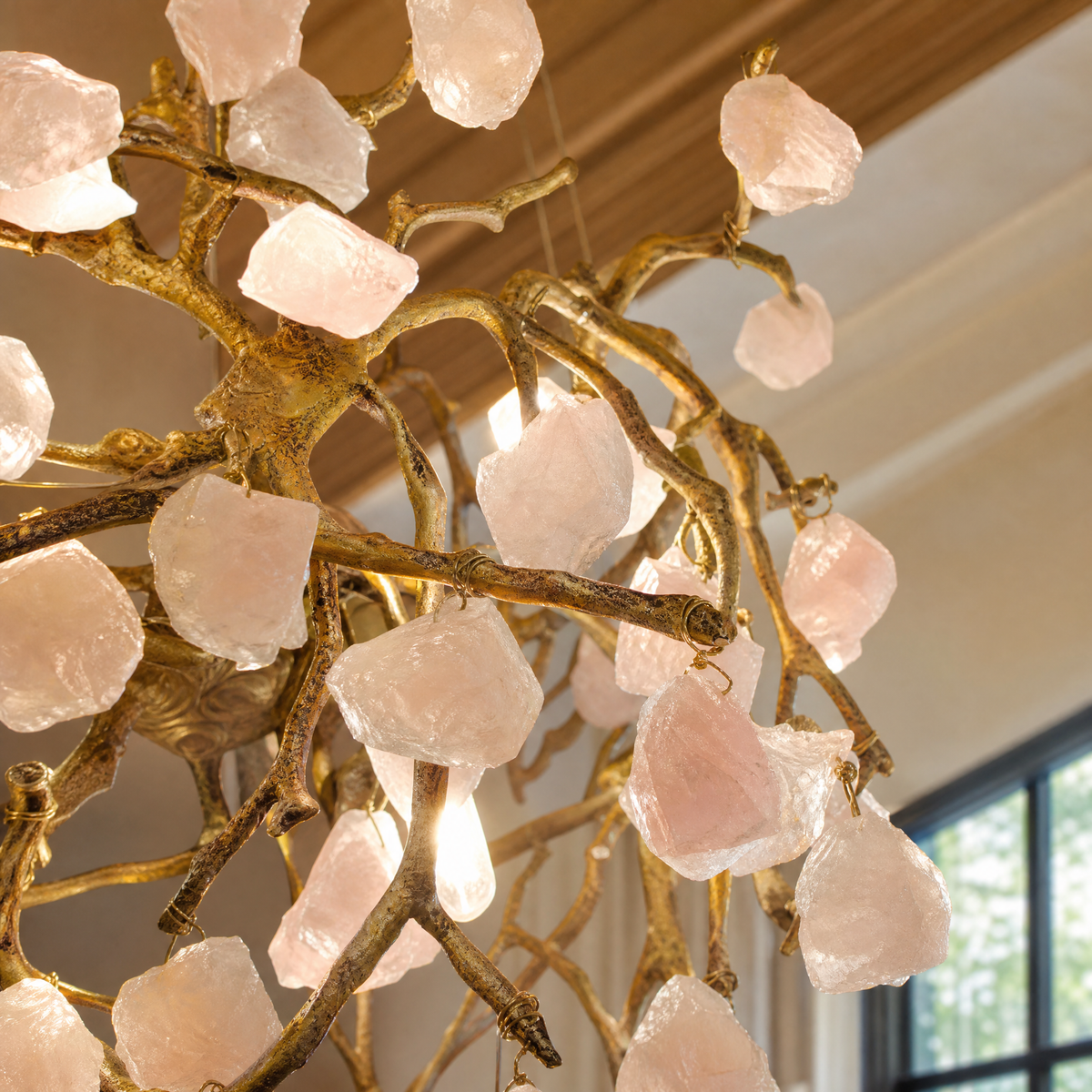 A branching metal chandelier finished in warm brass featuring clusters of raw rose quartz crystals.