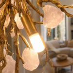 A modern branch chandelier with a textured gold finish features suspended raw rose quartz crystals casting a warm glow.