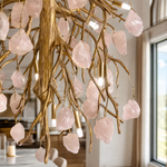 A modern branch chandelier with a textured gold finish features suspended raw rose quartz crystals casting a warm glow.