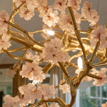 A circular gold metal ring chandelier decorated with pink crystal floral blooms and internal G9 light sockets.