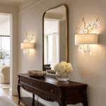 A gold metal branch wall sconce with clear crystal songbird accents and an off-white fabric drum shade.