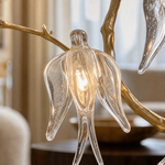 A gold metal branch wall sconce with clear crystal songbird accents and an off-white fabric drum shade.
