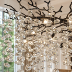 A modern matte black metal branch chandelier adorned with cascading clear crystal drops in a circular shape.
