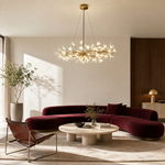 A long gold metal chandelier features white petal-shaped glass shades arranged in an organic branch silhouette.