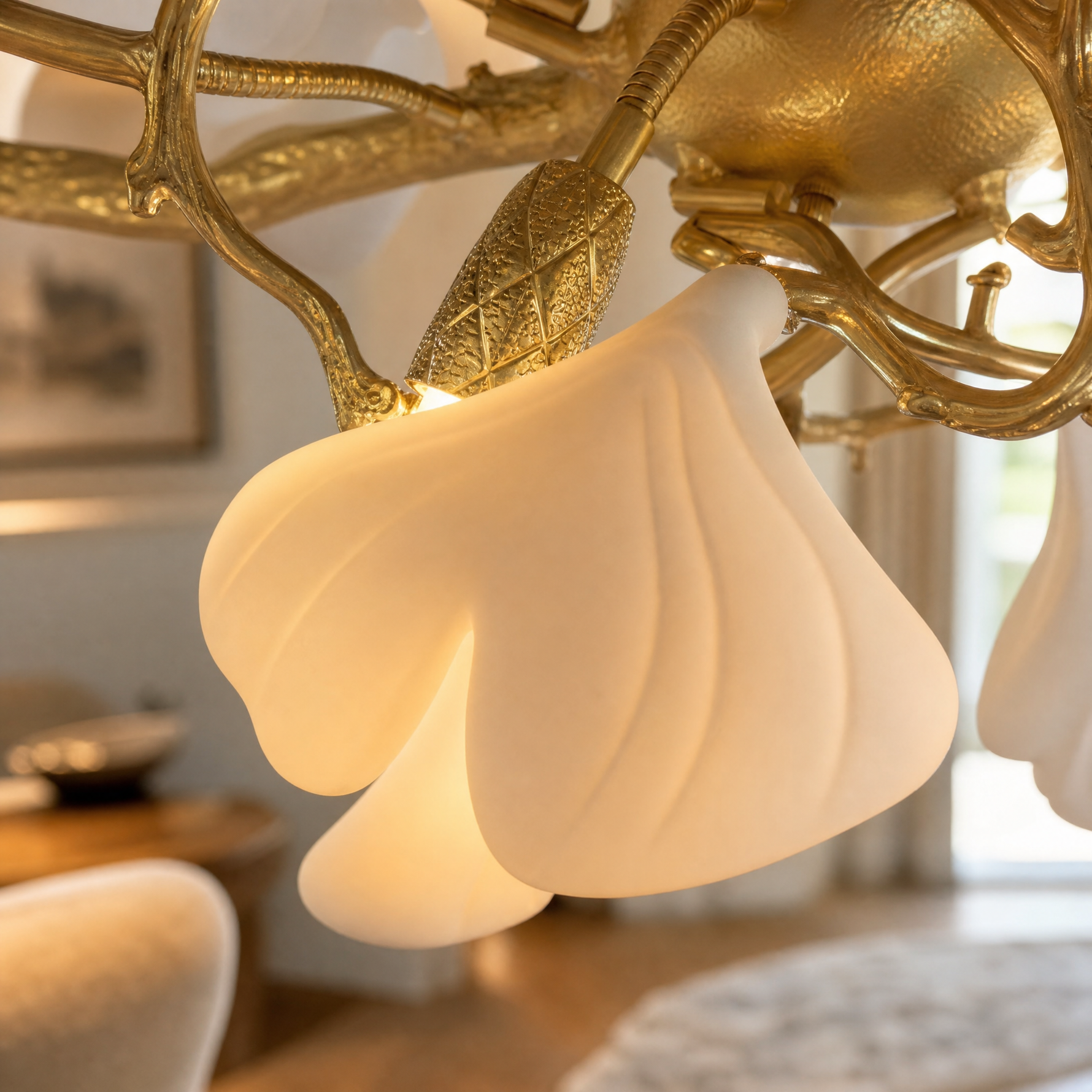 A long gold metal chandelier features white petal-shaped glass shades arranged in an organic branch silhouette.