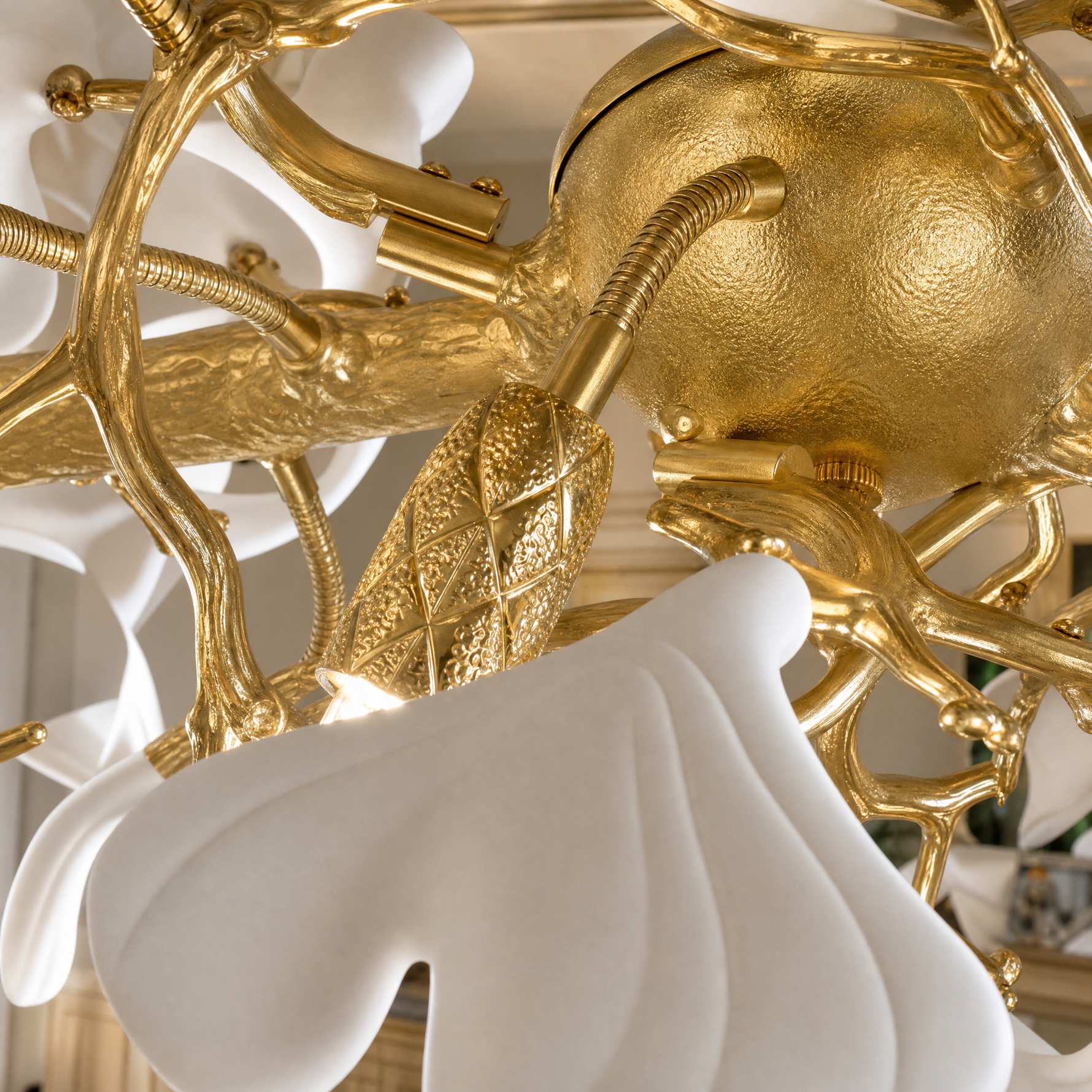 A long gold metal chandelier features white petal-shaped glass shades arranged in an organic branch silhouette.