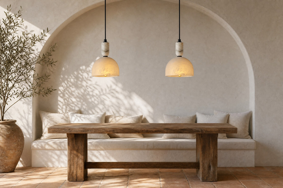Two black Alabaster Shade pendants above a rustic oak table in a sunlit whitewashed arched dining nook with a linen-cushioned bench and an olive tree