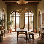 Yiosi Cascading Copper flush mount ceiling chandelier over rustic Mediterranean dining table with arched terrace doors and olive trees